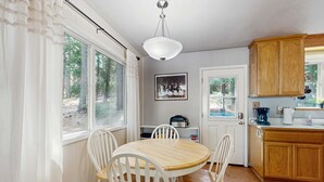 A kitchen with a round wooden table, white chairs, a hanging light fixture, wooden cabinets, and a door leading outside. - Cozy, dog-friendly cabin with large private deck, fireplace, BBQ-close to trails (South Lake Tahoe)