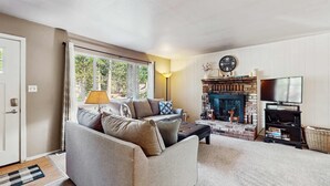 A living room with a sofa, a fireplace, a television, and a clock on the wall. - Cozy, dog-friendly cabin with large private deck, fireplace, BBQ-close to trails (South Lake Tahoe)