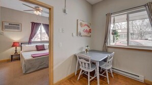 Une pièce comprenant un lit, une table avec des chaises, un ventilateur de plafond, une fenêtre avec des rideaux et un climatiseur fixé au mur.
