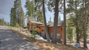 A cabin with a stone-paved driveway, surrounded by tall pine trees. - Spacious home with private hot tub & game room - near skiing, hiking, biking (Truckee)