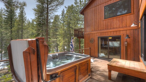 A wooden deck with a hot tub, a bench, and a view of a forest. - Spacious home with private hot tub & game room - near skiing, hiking, biking (Truckee)