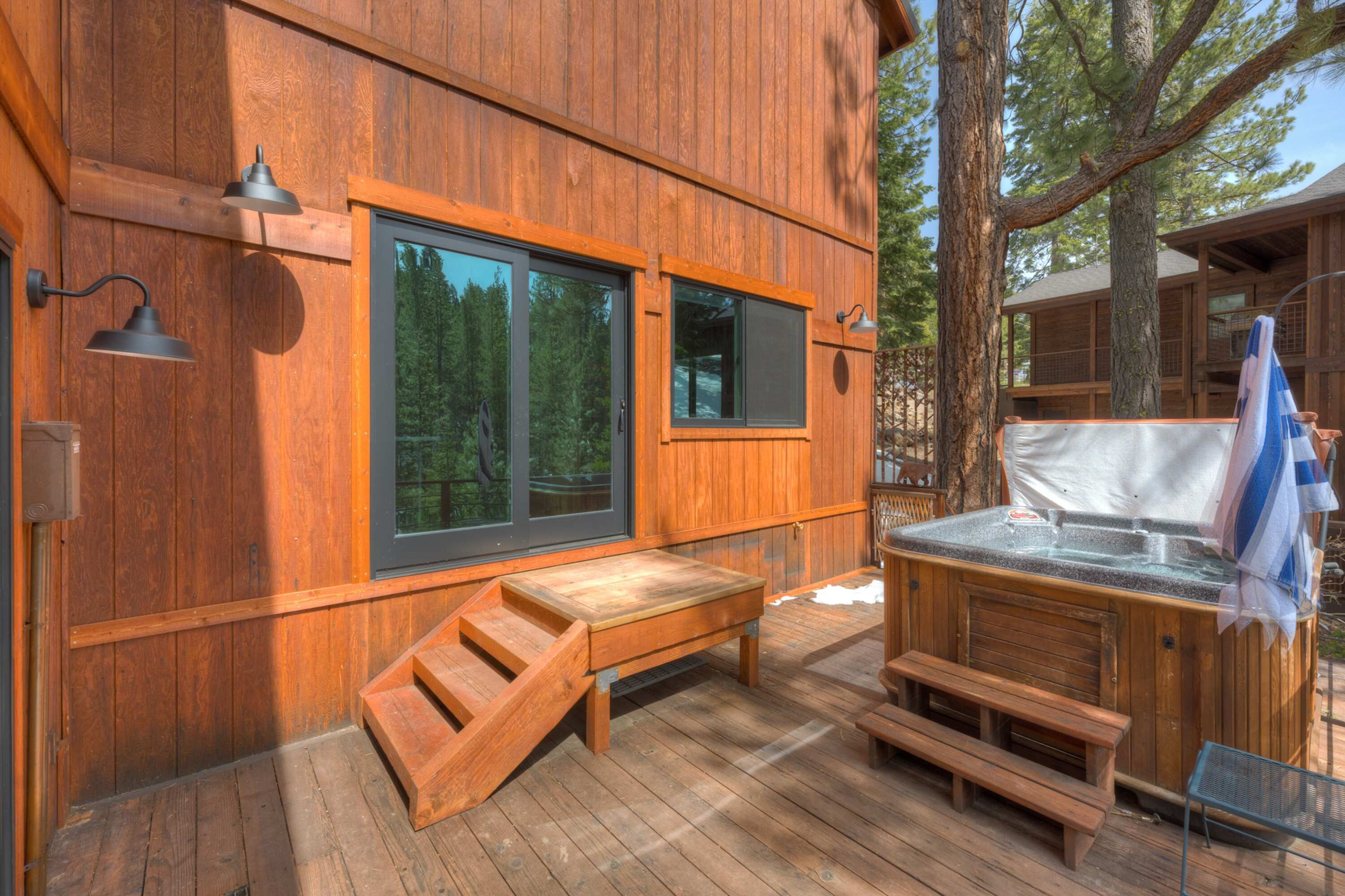 A wooden cabin with a hot tub, wooden deck, and a large window.