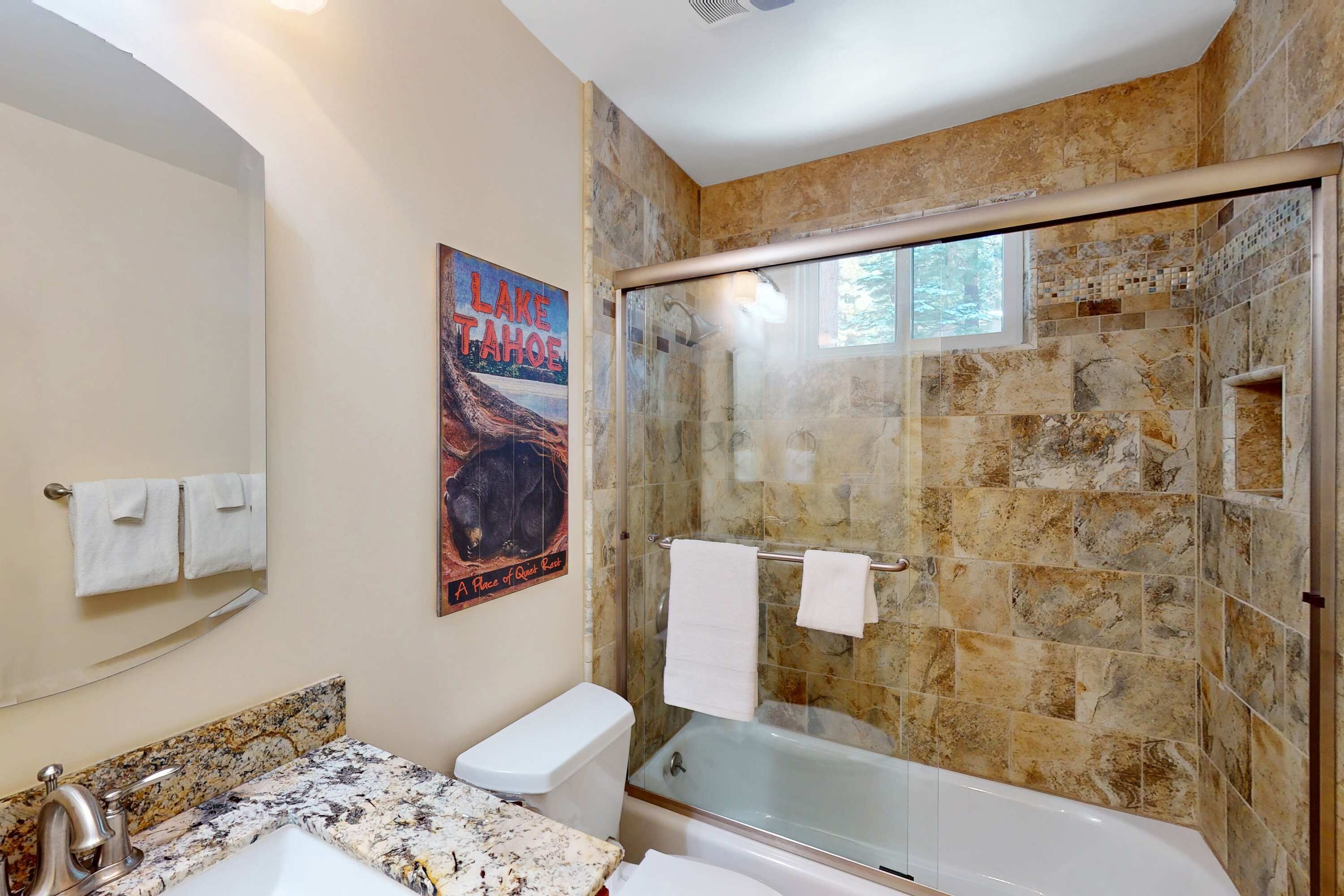 A bathroom with a granite countertop, a toilet, a glass-enclosed shower, and a poster on the wall.