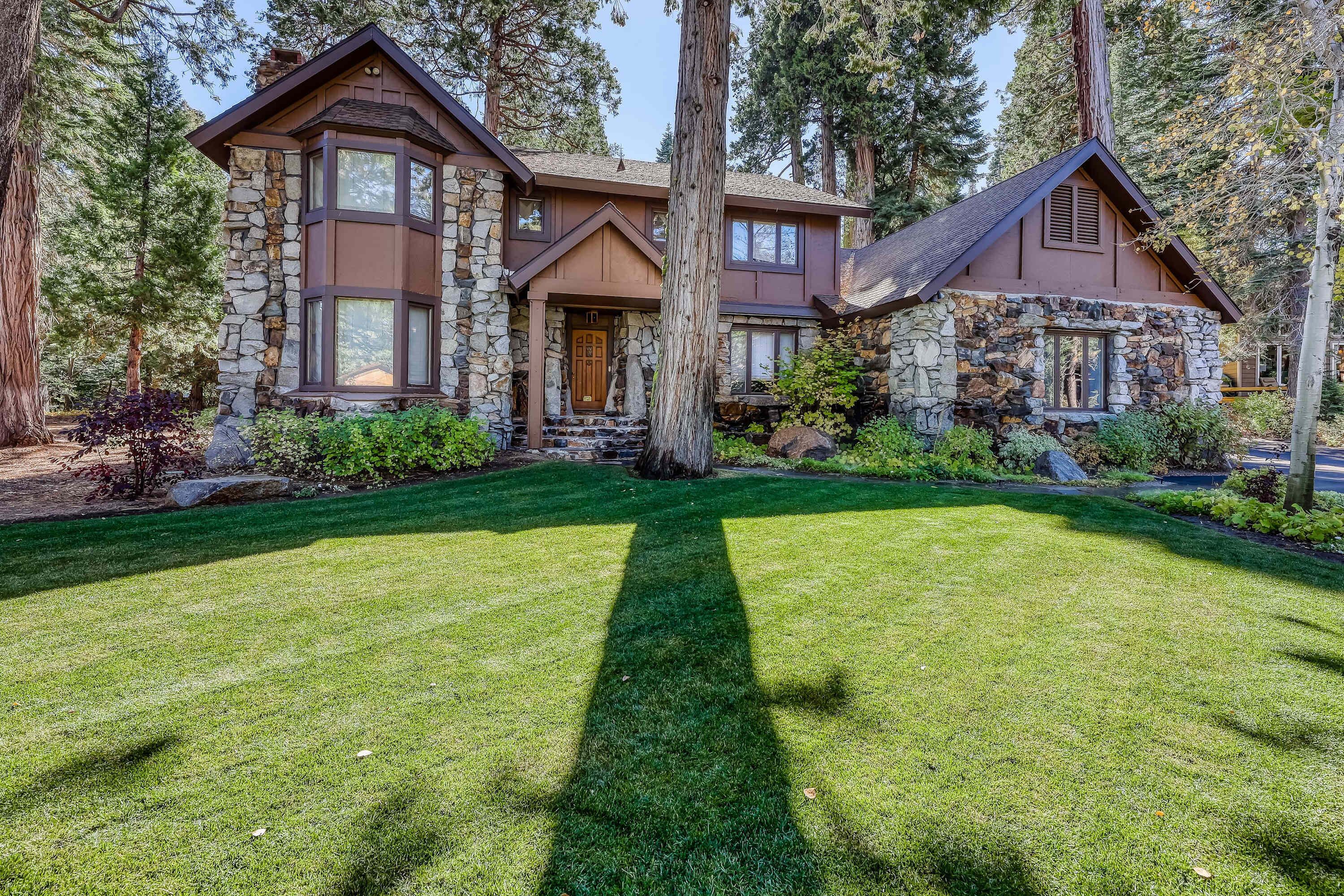 A two-story house with stone and wood exterior, a well-maintained lawn, and tall trees surrounding the property.
