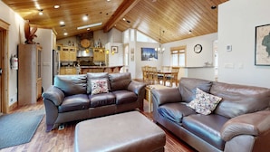 A spacious living area with leather sofas, wooden ceiling beams, and a kitchen in the background. - Immaculate Dog-Friendly Home with Private Hot Tub, Billiards, 2 Jacuzzi Tubs (South Lake Tahoe)