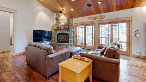 A living room with a stone fireplace, leather sofas, a wooden coffee table, and a television. - Immaculate Dog-Friendly Home with Private Hot Tub, Billiards, 2 Jacuzzi Tubs (South Lake Tahoe)