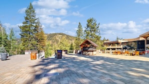 Ein gepflasterter Außenbereich mit einer Holzhütte, einem Gebäude mit großen Fenstern und einem Berg im Hintergrund.