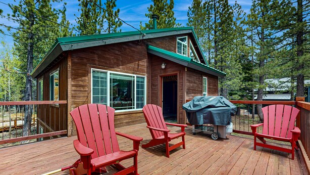 Eine Holzhütte mit einer Terrasse, zwei Adirondack-Stühlen und einem Grill.
