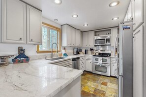 Una cocina moderna con armarios blancos, electrodomésticos de acero inoxidable, encimera de mármol y suelo de baldosas con diseño.