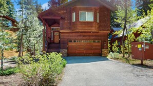 Eine zweistöckige Holzhütte mit Garage, umgeben von Bäumen.