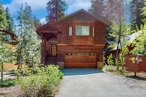 Eine zweistöckige Holzhütte mit Garage, umgeben von Bäumen.
