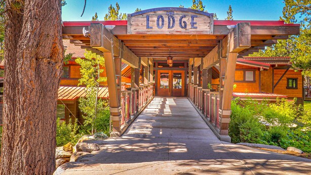 A lodge entrance with a wooden archway, a pathway leading to the building, and a tree to the left. - Dog-friendly snowbird escape with pool, hot tub & sauna access, & woodstove (Truckee)