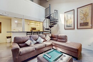 A spacious living area with a leather sofa, a coffee table, a spiral staircase, and framed artwork on the walls. - Condo with pool, hot tub & lake access (South Lake Tahoe)