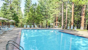A swimming pool surrounded by tall trees, with lounge chairs and umbrellas. - Inviting condo with balconies, fireplace, outdoor pool, sauna, & fitness center (Kings Beach)