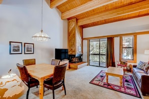 A spacious living room with a wooden ceiling, a fireplace, a television, and a large window. - Northstar condo close to skiing with pool, hot tub, gym, game room & W&D (Truckee)