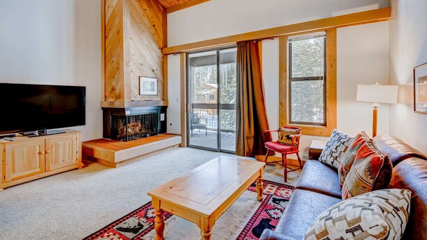 A living room with a fireplace, a television, a sofa, and a large window. - Northstar condo close to skiing with pool, hot tub, gym, game room & W&D (Truckee)