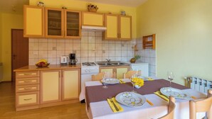 A compact kitchen with wooden cabinets, a gas stove, and a dining area set for two with a table set for a meal. - Cozy accommodation in quiet surroundings with sea view and barbecue (Dramalj)