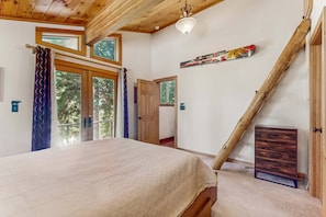 A bedroom with a bed, wooden ceiling beams, a window, and a door. - Modern Lux Cabin with Stunning Views, Spa, Large Kitchen and Dining, Fireplace (Carnelian Bay)