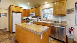 A kitchen with wooden cabinets, a granite countertop, a refrigerator, a microwave, a dishwasher, and a window with blinds. - Cozy, enchanting retreat with hot tub, stunning deck, & balcony - close to beach (Kings Beach)