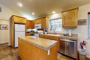 A kitchen with wooden cabinets, a granite countertop, a refrigerator, a microwave, a dishwasher, and a window with blinds.