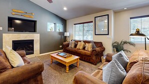 A living room with a fireplace, a ceiling fan, a television, and a large window with blinds. - Cozy, enchanting retreat with hot tub, stunning deck, & balcony - close to beach (Kings Beach)