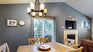 A dining area with a wooden table, chairs, a chandelier, a clock, a framed picture, and a fireplace. - Cozy, enchanting retreat with hot tub, stunning deck, & balcony - close to beach (Kings Beach)