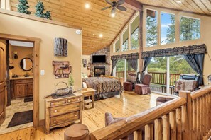 Ein geräumiges Wohnzimmer mit Kamin, Holzmöbeln und großen Fenstern, die einen Blick ins Freie bieten.