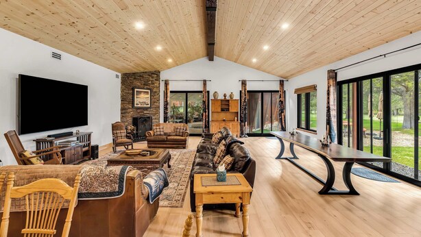 A spacious living room with a large flat-screen TV, leather sofas, wooden furniture, and a stone fireplace. - Large Luxury Estate Home on Golf Course with Private Indoor Heated Pool, Spa, Sauna (South Lake Tahoe)