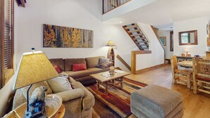 A spacious living area with a sofa, coffee table, and a lamp. A staircase leads to an upper level. - Vintage Ski Condo Close to Slopes with WiFi, Shared Pools & Hot Tub, & Tennis (NorthStar-Truckee)