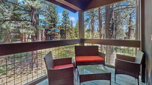 A covered balcony with wicker furniture and a glass table, overlooking a forested area. - Vintage Ski Condo Close to Slopes with WiFi, Shared Pools & Hot Tub, & Tennis (NorthStar-Truckee)