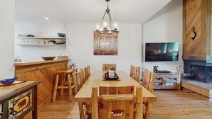 A dining area with a wooden table and chairs, a chandelier, a television, and a fireplace. - Vintage Ski Condo Close to Slopes with WiFi, Shared Pools & Hot Tub, & Tennis (NorthStar-Truckee)