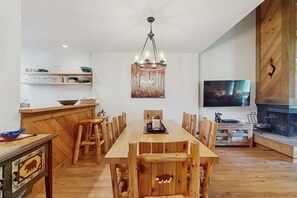 A dining area with a wooden table and chairs, a chandelier, a television, and a fireplace. - Vintage Ski Condo Close to Slopes with WiFi, Shared Pools & Hot Tub, & Tennis (NorthStar-Truckee)