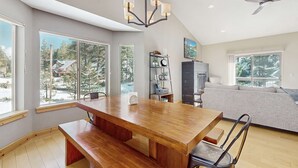 Un'ampia stanza con un tavolo da pranzo in legno, una ventola a soffitto e ampie finestre che si affacciano su alberi e una casa.