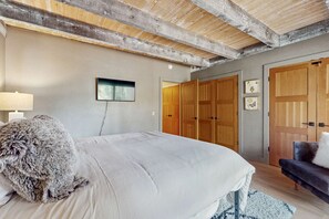 Ein Schlafzimmer mit einem Bett, einem flauschigen Kopfkissen, einer Nachttischlampe, einer Holzbalkendecke und einem Kleiderschrank.
