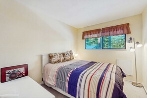 A bedroom with a bed, a window with curtains, a bedside lamp, and a framed picture on the wall. - Spacious Condo with Fireplace, Deck, Wet Bar, Pool, Free Shuttle to Ski Resort (Incline Village)