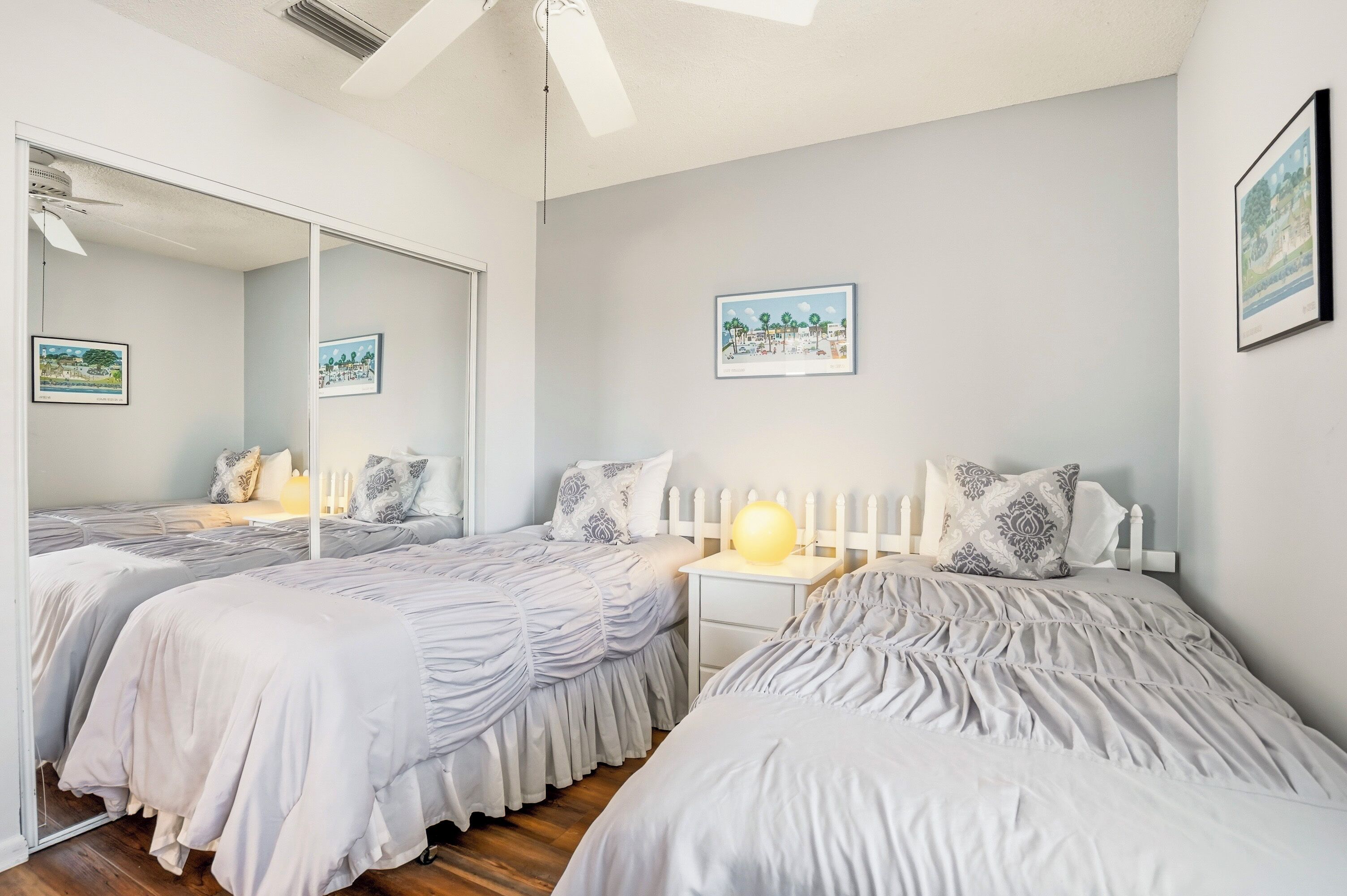A bedroom with two beds, a bedside table with a lamp, a mirror, and framed pictures on the wall.