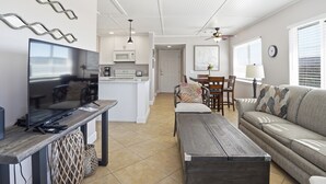Uma sala de estar moderna com televisão de tela plana, mesa de centro de madeira, sofá e área de jantar com mesa e cadeiras.