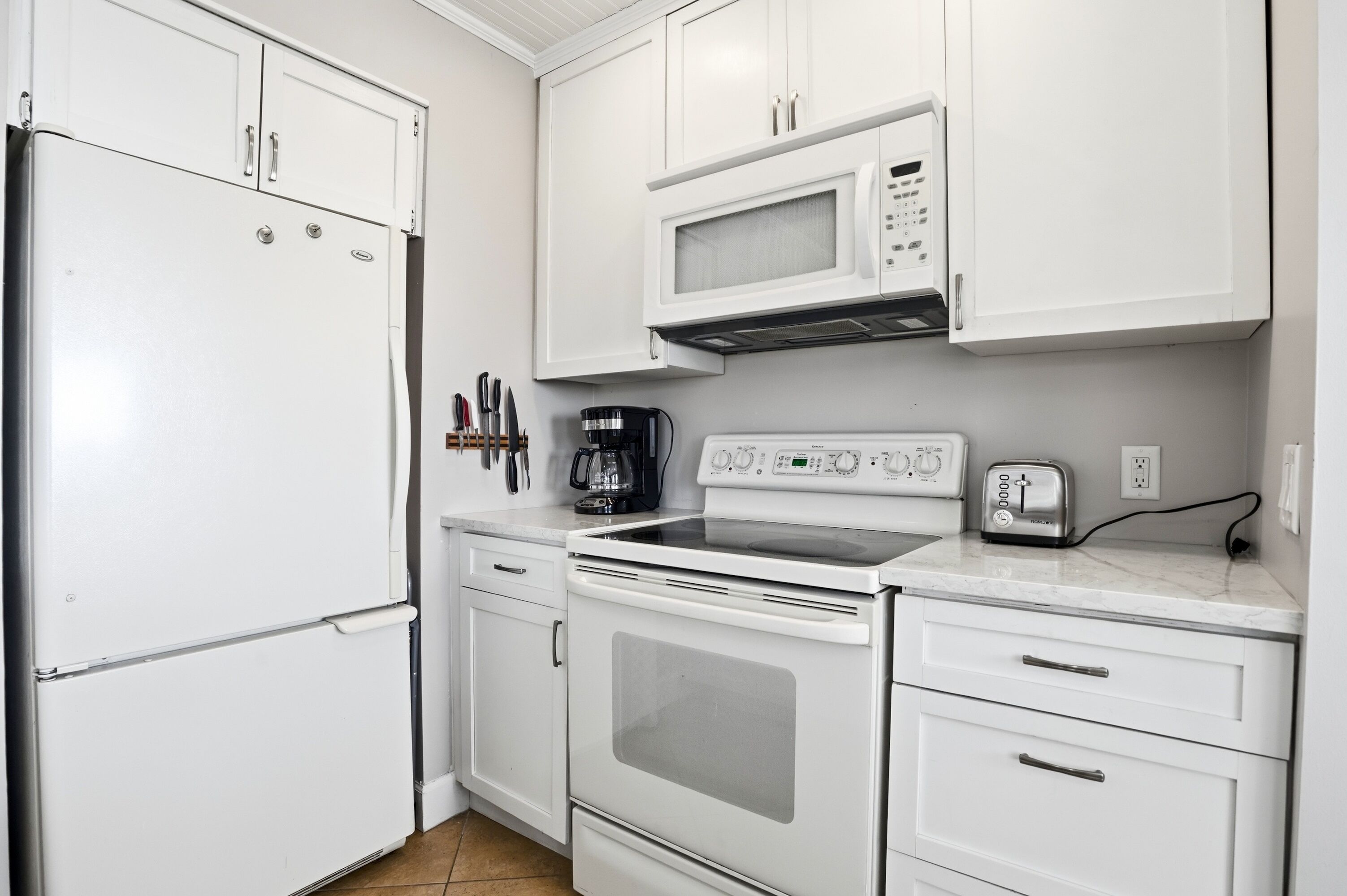A kitchen with white cabinets, a refrigerator, a microwave, a stove, and a toaster.