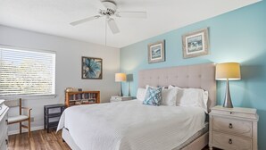 Quarto com cama, mesas de cabeceira, uma cadeira, estante e ventilador de teto.