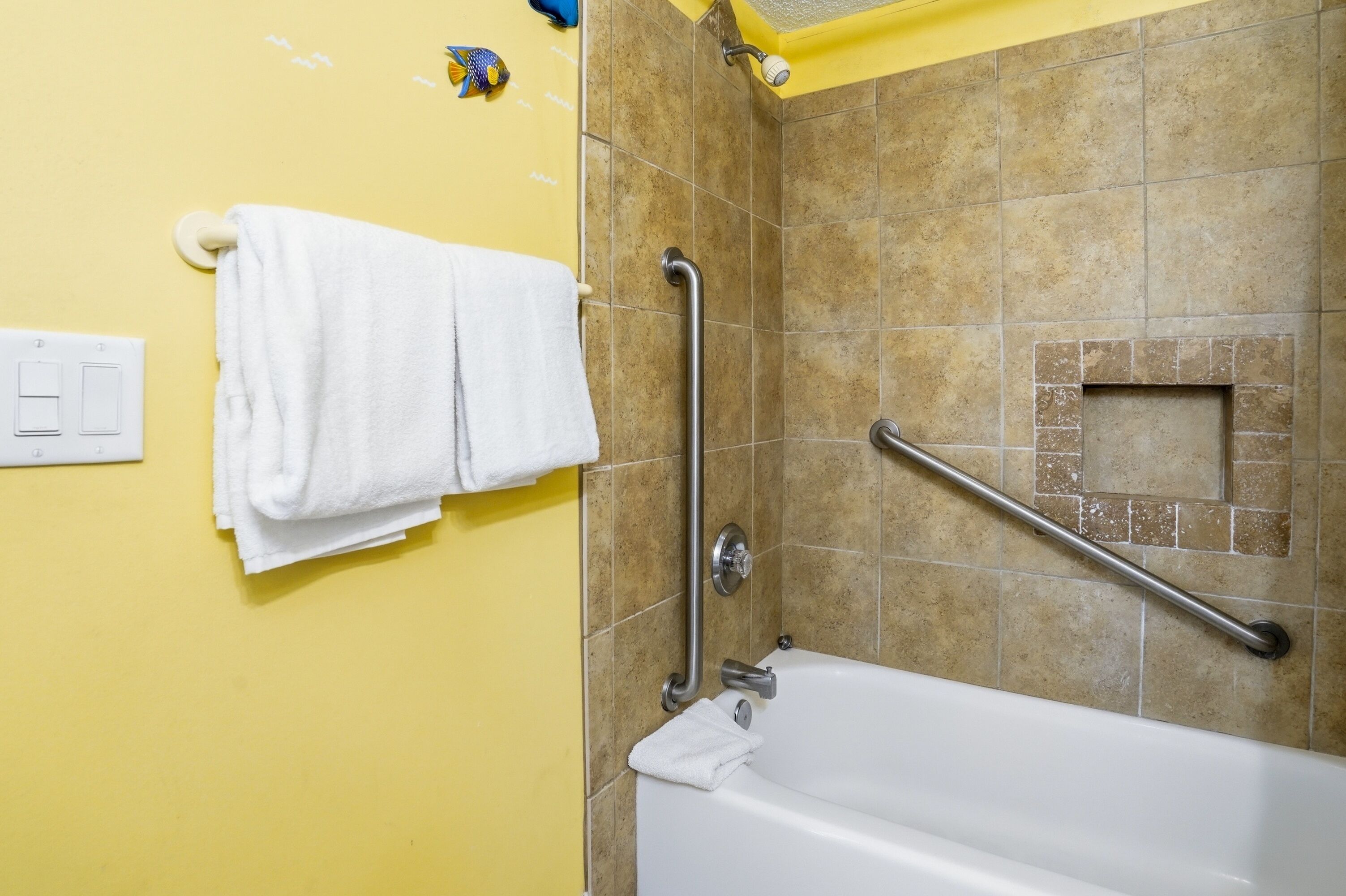 A bathroom with a bathtub, a handrail, a towel rack, and a shower area.
