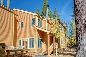 A two-story house with a chimney, a deck with chairs, and a staircase leading to the entrance.