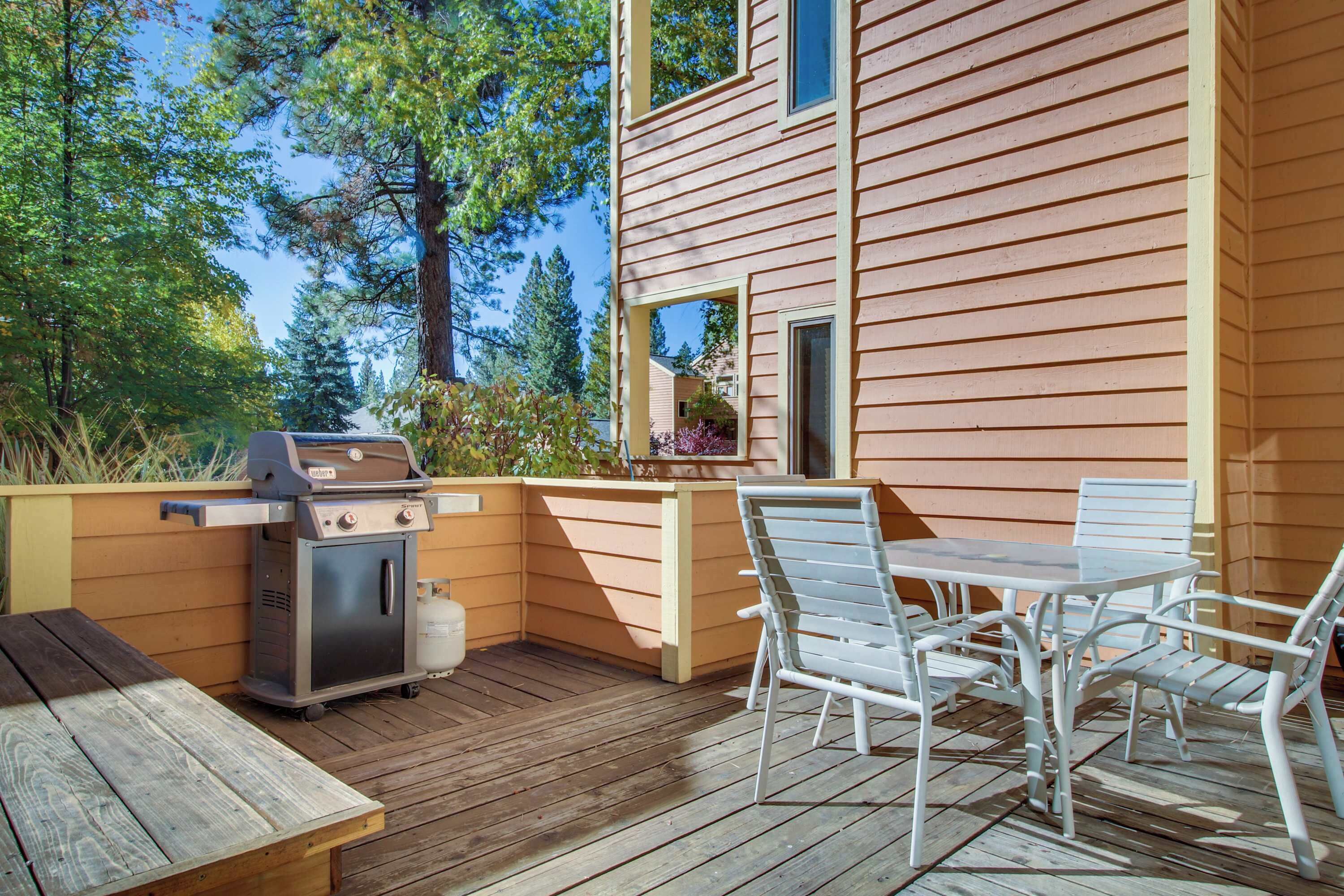 A wooden deck with a grill, a table with chairs, and a view of a house.