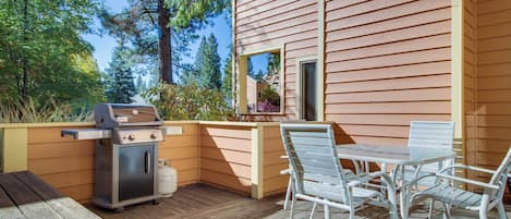 A wooden deck with a grill, a table with chairs, and a view of a house.