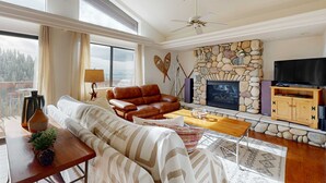 Una sala de estar con chimenea de piedra, sofá de cuero y televisor.