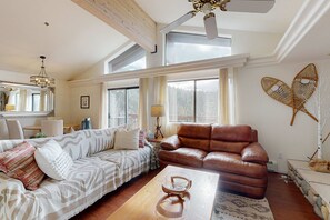 Ein geräumiges Wohnzimmer mit großem Fenster, Deckenventilator, braunem Ledersofa, gemustertem Sofa und einem Couchtisch aus Holz.