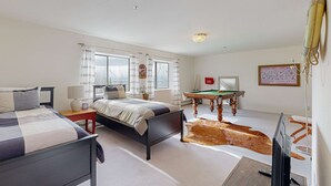 Un dormitorio con dos camas, una mesa de billar, una televisión y un ventanal grande con cortinas.