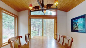 Un tavolo da pranzo in legno con sei sedie, ampie finestre e vista su una foresta.