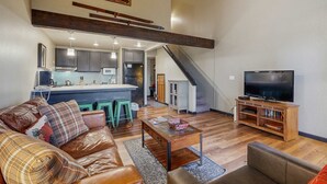 A spacious living area with a sofa, coffee table, and television. A kitchen with a bar is visible in the background. - Lakefront retreat with shared pool, hot tub, & sauna - near shopping & skiing (South Lake Tahoe)