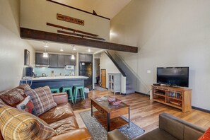 Ein geräumiger Wohnbereich mit Sofa, Couchtisch und Fernseher. Im Hintergrund ist eine Küche mit Bar zu sehen.