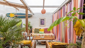 En hyggelig patio med et træbord, stole og en farverig stribet gardinbaggrund.